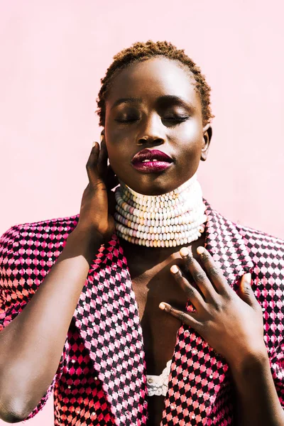 Pembe arka planda siyah derili güzel bir Afrika mankeni. Özgün bir gülümseme. Canlı renkler, şeker kolye. Yüksek kalite fotoğraf