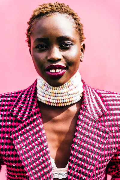 Pembe arka planda siyah derili güzel bir Afrika mankeni. Özgün bir gülümseme. Canlı renkler, şeker kolye. Yüksek kalite fotoğraf