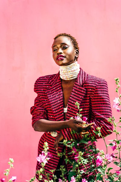 Pembe arka planda siyah derili güzel bir Afrika mankeni. Özgün bir gülümseme. Canlı renkler, şeker kolye. Yüksek kalite fotoğraf. Pembe çiçekler.
