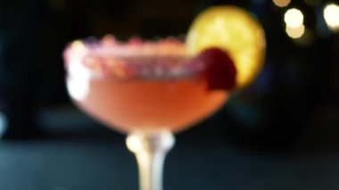 Yakın çekim, bir barda ferahlatıcı kırmızı bir kokteyl ve Kristal bardağı çiçekle süsleyen bir kadın eli..
