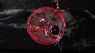 Kırmızı kiraz, ağır çekimde kokteyl bardağına düşüyor. 180 fps. Sıvılar sıçrıyor.