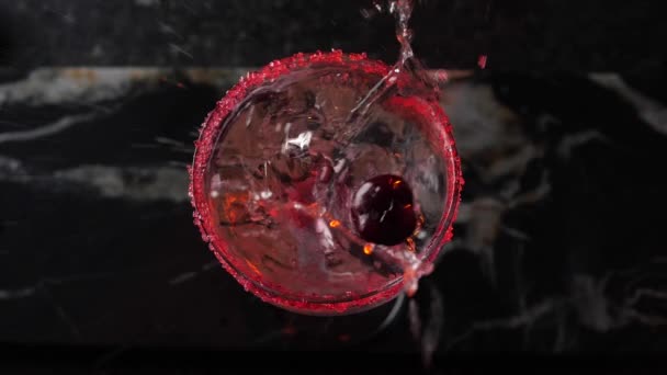Czerwona wiśnia wpada do kieliszka w ekstremalnym zwolnionym tempie. 180 fps. Rozpryskiwanie cieczy. — Wideo stockowe