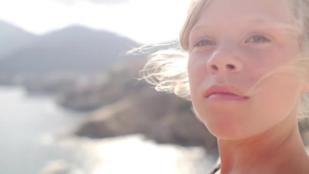 Barnet tittar över havet i sommarsolen och ler mot linsen. Obekymrad. — Stockvideo