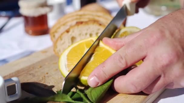 Cortar una naranja en el sol de verano en un entorno al aire libre. Familia desayunando. Primer plano. — Vídeos de Stock