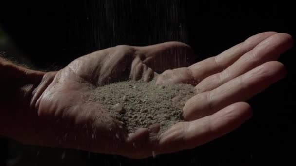 Zand valt in de hand van een man. Zwarte achtergrond. Slow-motion 180 fps. De vier elementen. — Stockvideo