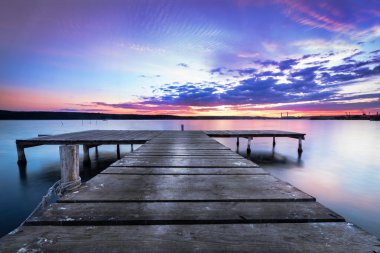 Wooden pier on a blue lake sunset and smooth reflection on water clipart