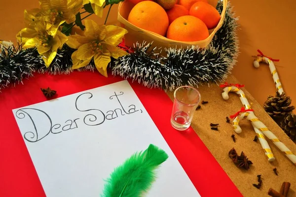 Christmas postcard: Desk with a letter to Santa Claus surrounded by candy canes, tinsel, nails, a basket of oranges and golden poinsettias