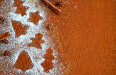 Zencefilli ekmek adam, çanlar, noel ağaçları ve yıldızlı siluetler ahşap bir zemin üzerine serpiştirilmiş şeker ve tarçın çubukları, yıldız anason ve karanfil serpiştirilmiş.