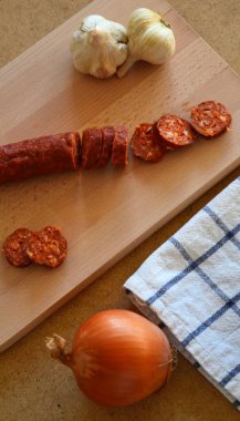 Beyaz mavi bir kareli kumaş üzerinde dilimlenmiş bir tabak sucuğun yanında birkaç kızarmış tavuk parçaları. 