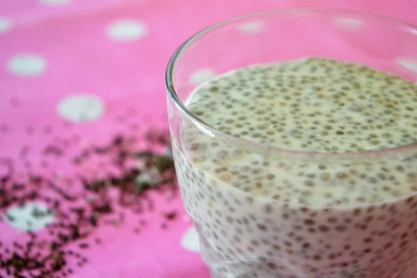 Chia seed and coconut milk pudding on a pink tablecloth with white polka dots surrounded by seeds and desiccated coconut