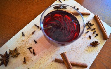 Baharatlı baharatlı şaraplar, yıldız anason, tarçın çubukları, karanfil ve kozalaklarla çevrili ahşap bir arka planda.