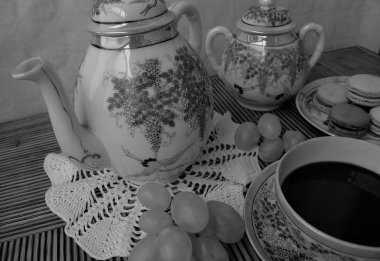 Porselen sette bir fincan çay ve ahşap bir masada üzümlerle çevrili bir tabak badem kurabiyesi.