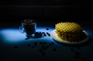 Ahşap arka planda bir fincan kahve ve waffle ile sakin bir hayat. Fotoğraf hafif anahtarla çekilmiş..