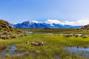 Karlı dağlarla dolu bir çayırda akan bir dere.