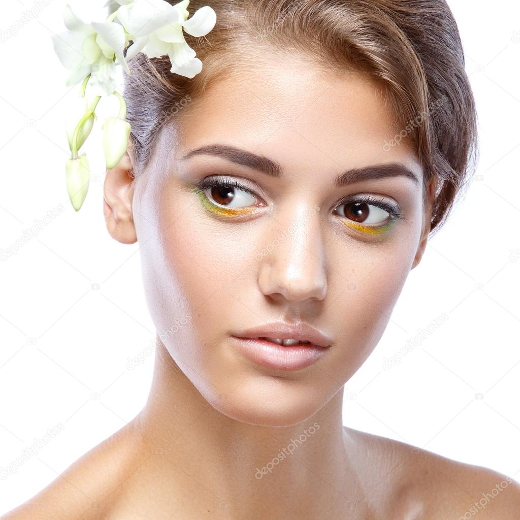 Young woman with clear face natural make up her hair up with a white flower on a light background
