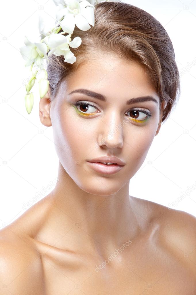 Young woman with clear face natural make up her hair up with a white flower on a light background