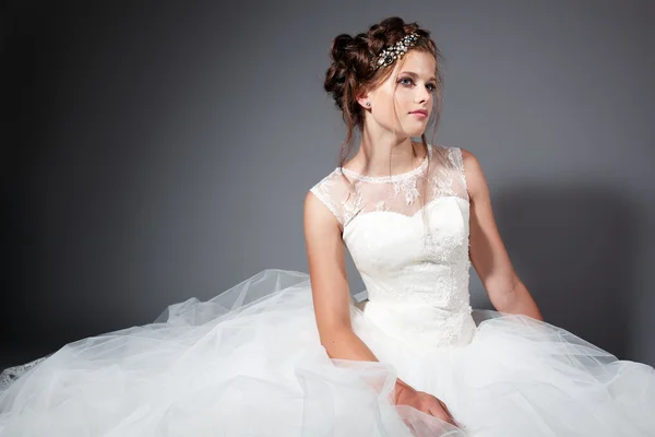 Mooie jonge bruid in een witte bruiloft jurk op de grijze stijlvolle achtergrond — Stockfoto