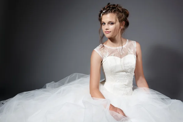 Mooie jonge bruid in een witte bruiloft jurk op de grijze stijlvolle achtergrond — Stockfoto