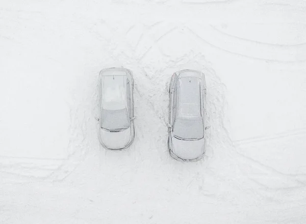Frozen car and SUV at winter season. Aerial top down view of the two snow-covered vehicles parked on snow surface after blizzard. White landscape, cold weather.