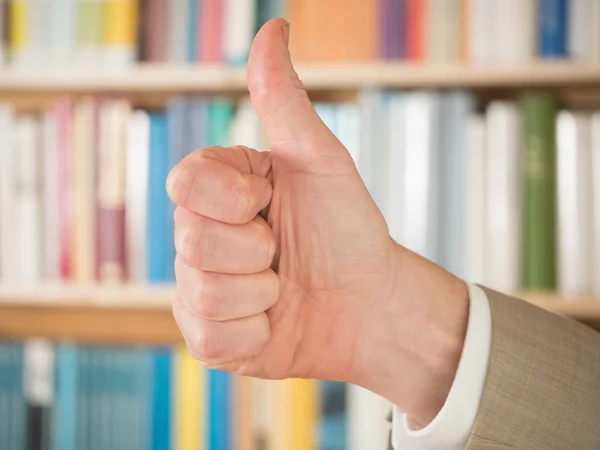 Thumbs up in front of bookshelf — Stock Photo, Image