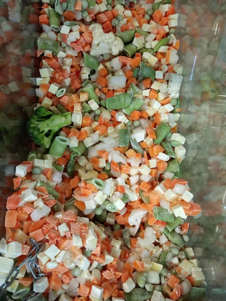 Donmuş sebzeler havuç, patates, fasulye, lahana, sebze reyonundaki plastik bir kabın içindeki yeşil bezelyeler.