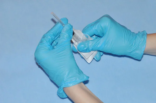 Aşılama. Koruyucu eldiven giyen bir doktor mavi arka planda bulunan bir hastayı koronavirüse karşı aşılamak için şırınga açar.