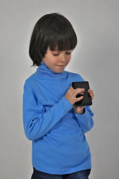 Çocuklar için mobil uygulama. Cep telefonunu işaret eden, kameraya gülümseyen ve telefonu gösteren mutlu, neşeli, küçük bir çocuk. Gri arka planda izole edilmiş kapalı stüdyo çekimi