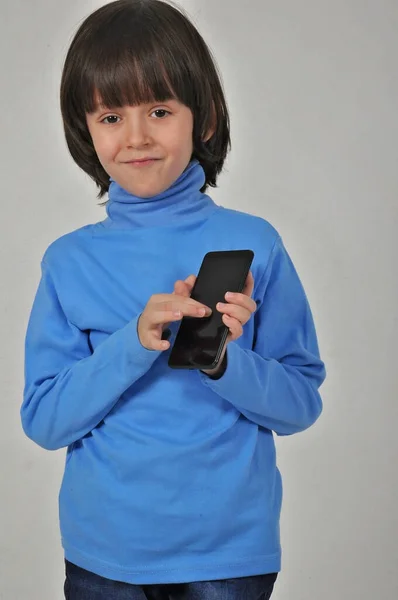 Çocuklar için mobil uygulama. Cep telefonunu işaret eden, kameraya gülümseyen ve telefonu gösteren mutlu, neşeli, küçük bir çocuk. Gri arka planda izole edilmiş kapalı stüdyo çekimi