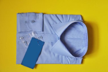 Yeni kumaş, erkek açık mavi gömleğini sarıya sarmış. Gömlek satılık. İzole edilmiş gömlek. İşçilik için konsept kıyafet