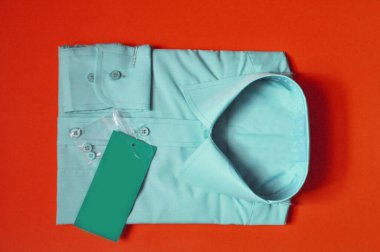 Tekstil kumaşının satış öncesi hazırlığı. Yeni kumaş, erkek açık mavi gömleğini kırmızı arka planda paketlemiş. Gömlek satılık. İzole edilmiş gömlek. İşçilik için konsept kıyafet