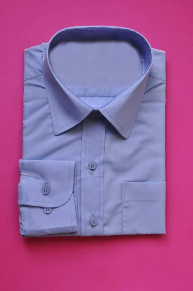 Yeni kumaş, erkek açık mavi gömleğini pembe arka planda paketledi. Gömlek satılık. İzole edilmiş gömlek. İşçilik için konsept kıyafet