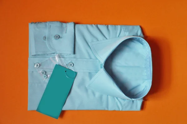Tekstil kumaşının satış öncesi hazırlığı. Yeni kumaş, turuncu arka planda açık mavi erkek gömleği paketlemiş. Gömlek satılık. İzole edilmiş gömlek. İşçilik için konsept kıyafet