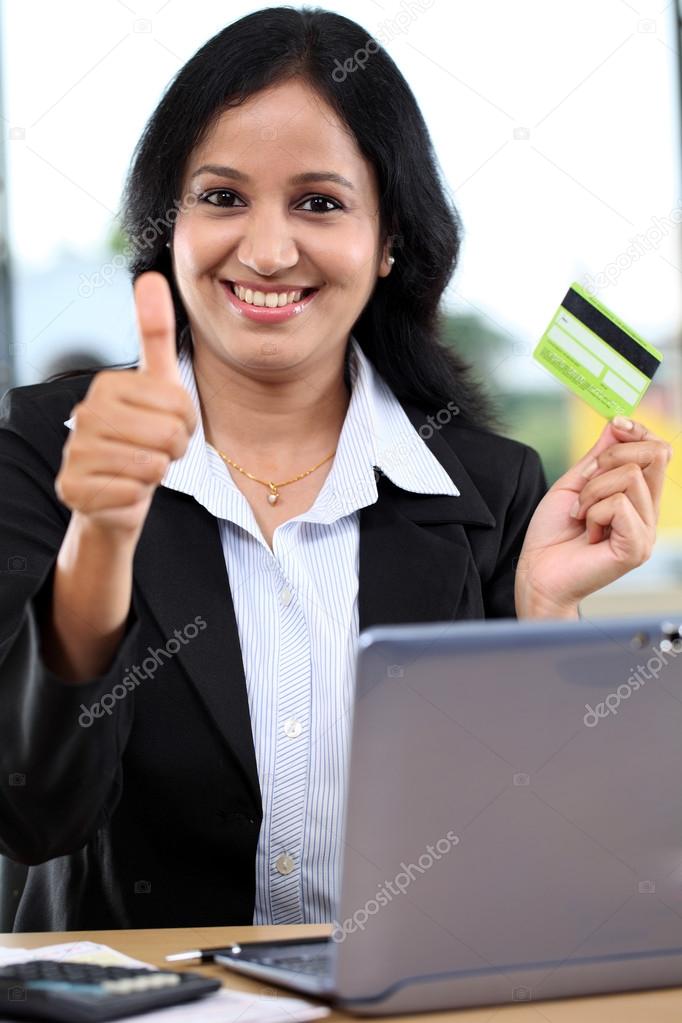 Businesswoman holding credit card and showing thumbs up gesture