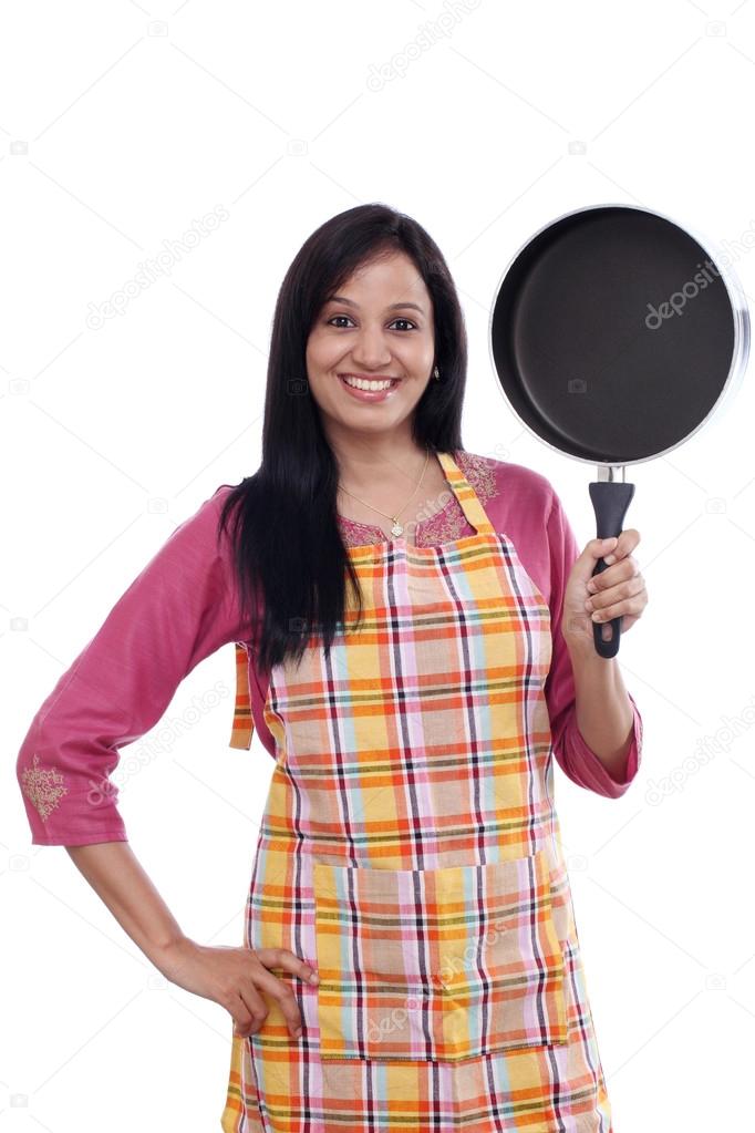 Young Indian woman holding kitchen utensil against white