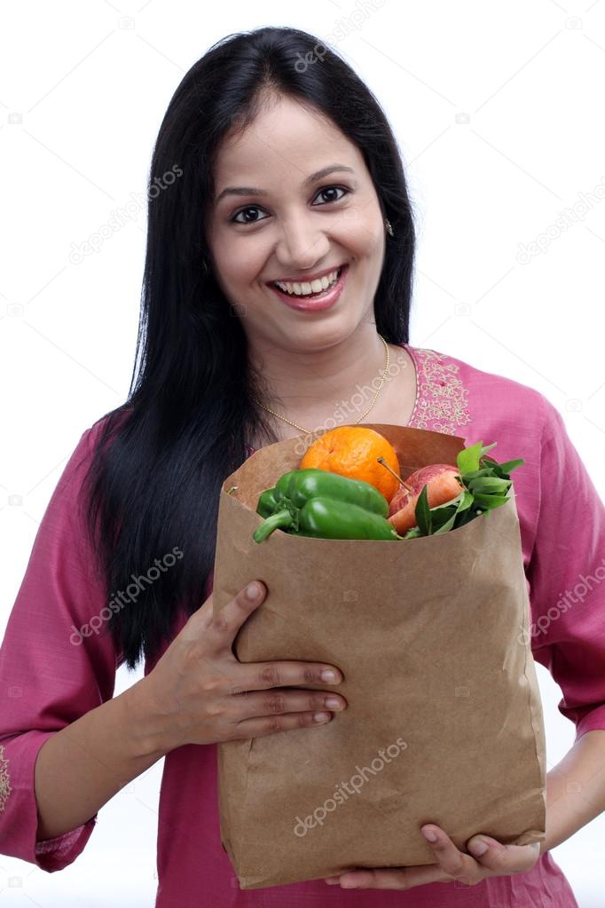 Young Indian woman holding grocery bag with full of fruits and v