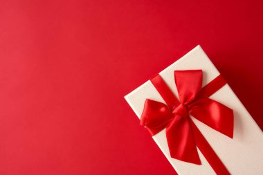 Kırmızı arka planda kırmızı kurdeleli beyaz hediye. Bayramlar için şenlikli zemin: Doğum günü, Sevgililer Günü, Noel, Yeni Yıl.