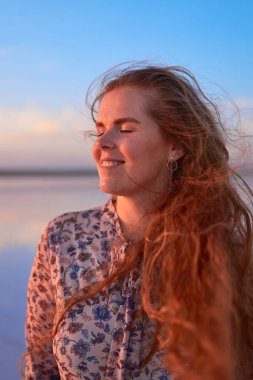 Uçan kızıl saçlı güzel, gülümseyen genç bir kadın.