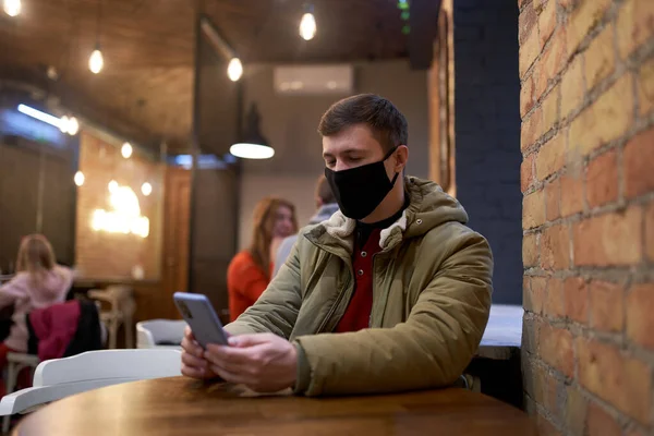 Caucasian man in cafe with protective face mask and phone
