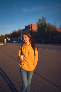 Beautiful caucasian young woman drinking coffee outdoors in yellow sweater