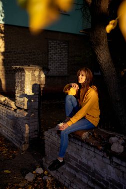 Beautiful caucasian young woman drinking coffee outdoors in yellow sweater