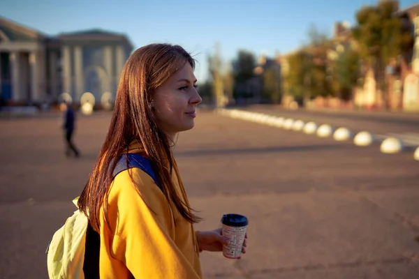 Beautiful caucasian young woman drinking coffee outdoors in yellow sweater