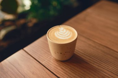 Bir bardak kapuçino ve ahşap masada latte sanatı. Güzel köpük ve seramik bardak.