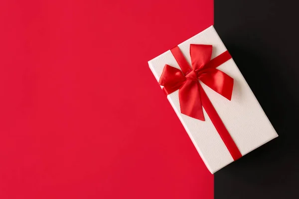 Білий подарунок з червоною стрічкою на яскраво-червоному тлі — стокове фото