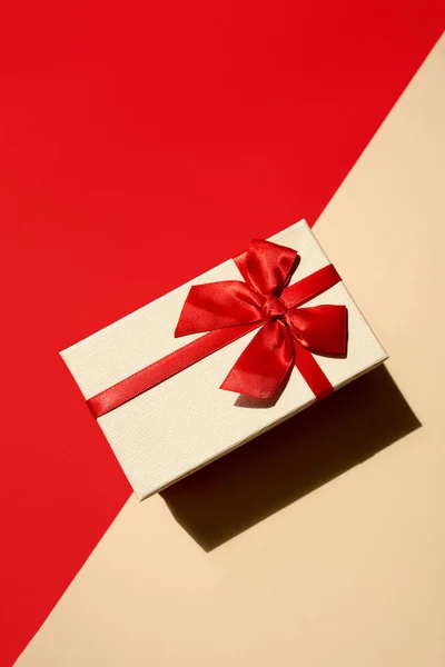 Weißes Geschenk mit roter Schleife auf leuchtend rotem Hintergrund — Stockfoto