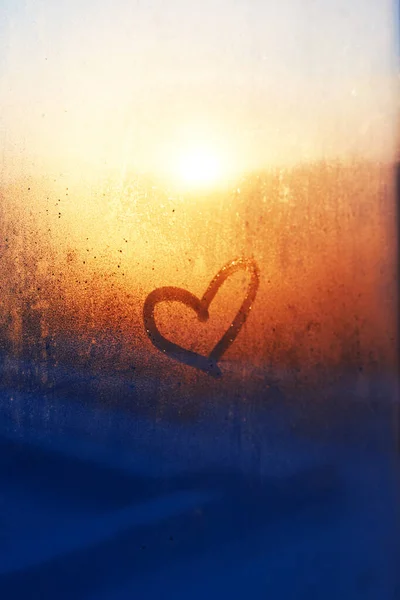 Heart drawn on a misty window and sunset on the background