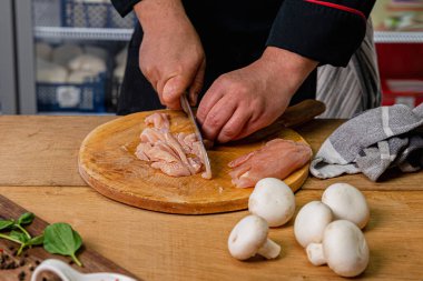 Şef yanında mantar olan tahta bir helikopterde tavuk göğsü dilimliyor..