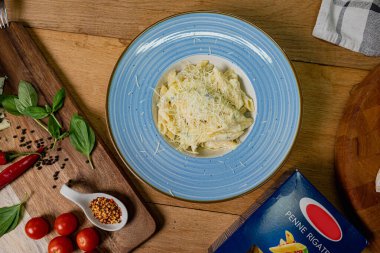 Penne Quatro Formaggi ahşap masada, yanında malzemeler var. İtalyan yemeği..
