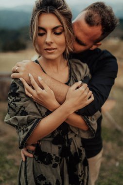 A close up portrait of a charming young couple laughing while man is embracing her wife outdoor in nature.