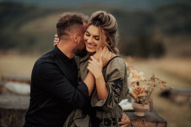 A close up portrait of a charming young couple laughing while man is embracing her wife outdoor in nature.