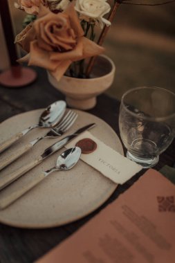 Dışarıda stilize edilmiş düğün masası, özel çiçek ve seramik düzenlemeler, mumlar ve çatal bıçak takımı..